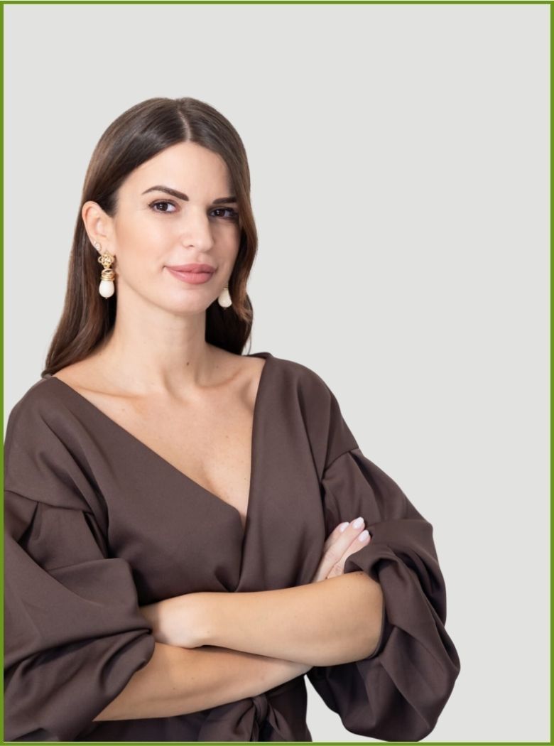 Donna con camicetta marrone e braccia incrociate, in posa su uno sfondo chiaro.
