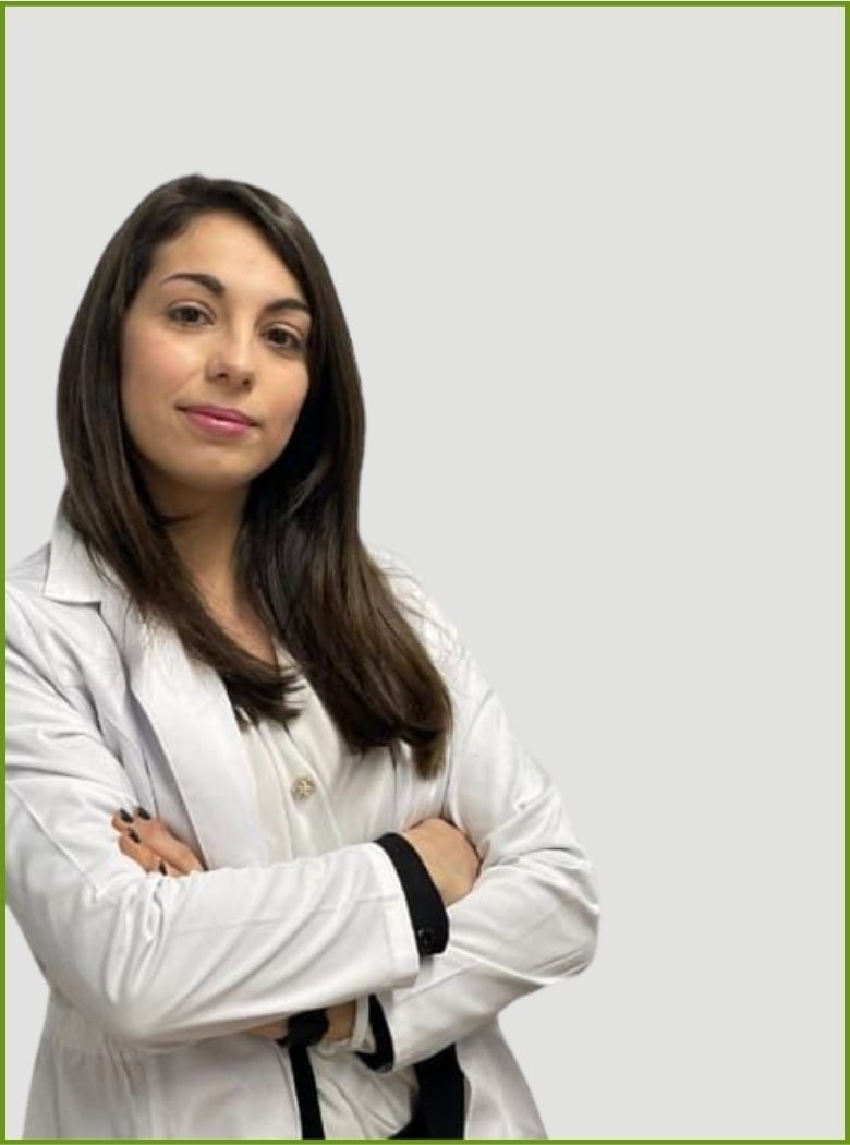 Persona in camice bianco con le braccia incrociate, in piedi davanti a uno sfondo chiaro e uniforme.