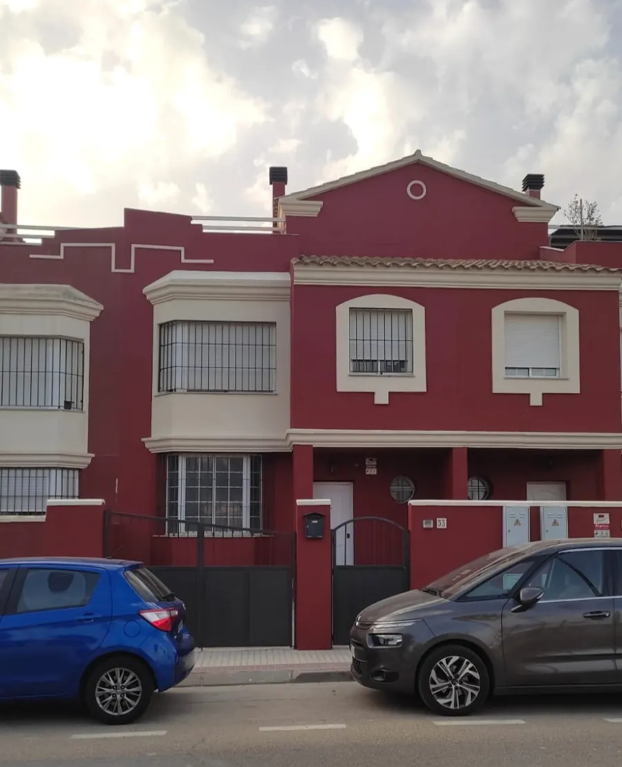 Casas adosadas rojas con coches azules y grises aparcados en una calle residencial.