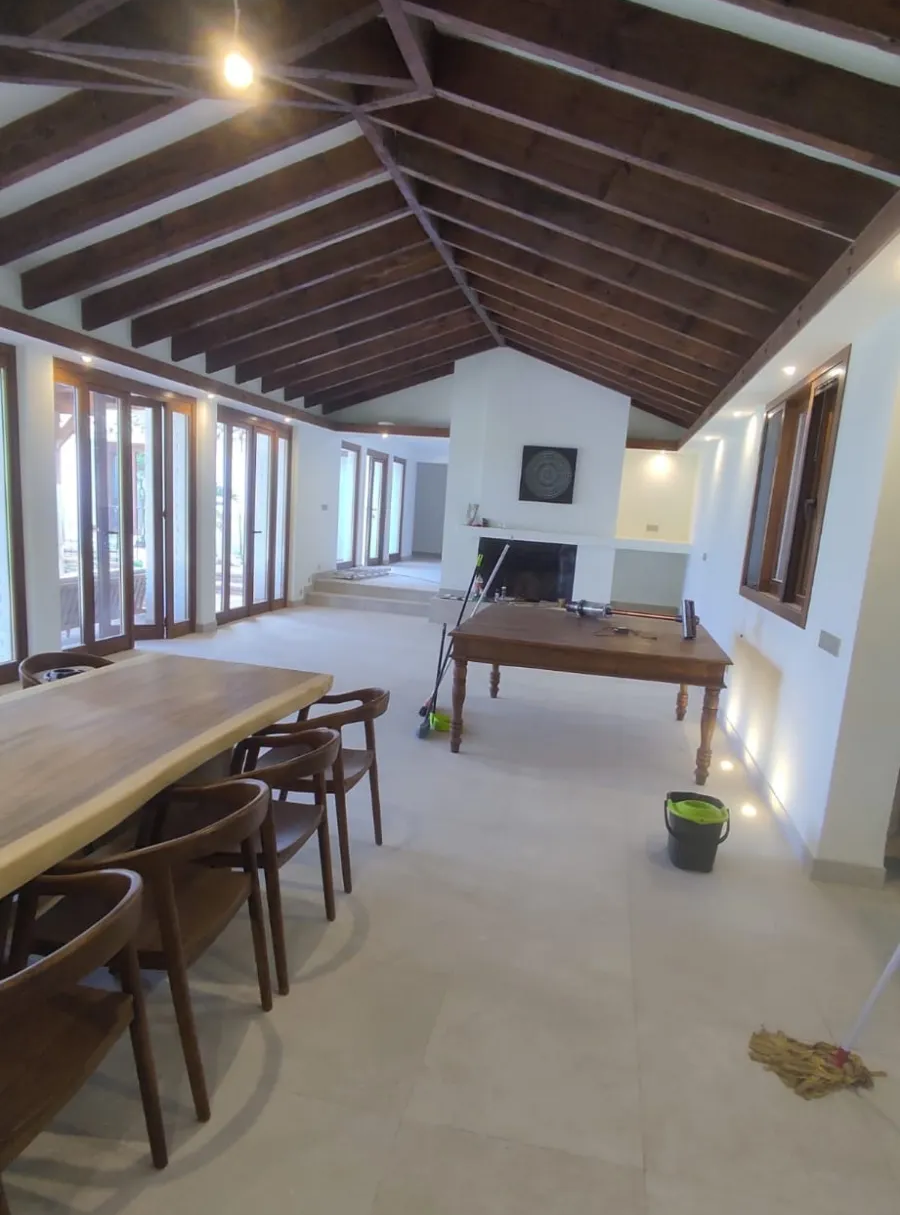 Comedor rústico vacío con mesas y sillas de madera, techo con vigas a la vista e iluminado por ventanas y apliques de pared.