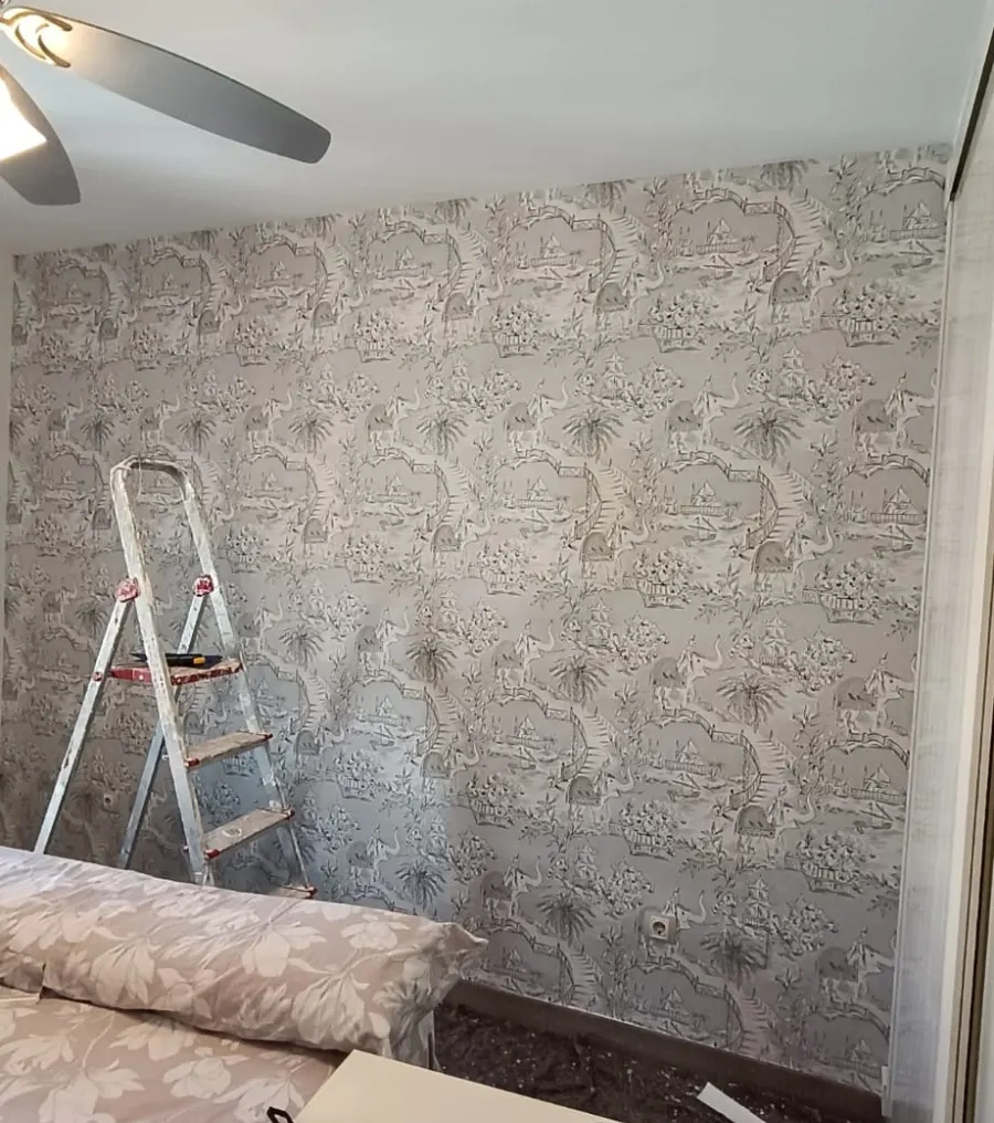 Sala de estar con papel tapiz estampado, escalera de mano, ventilador de techo y un sofá en proceso de renovación.