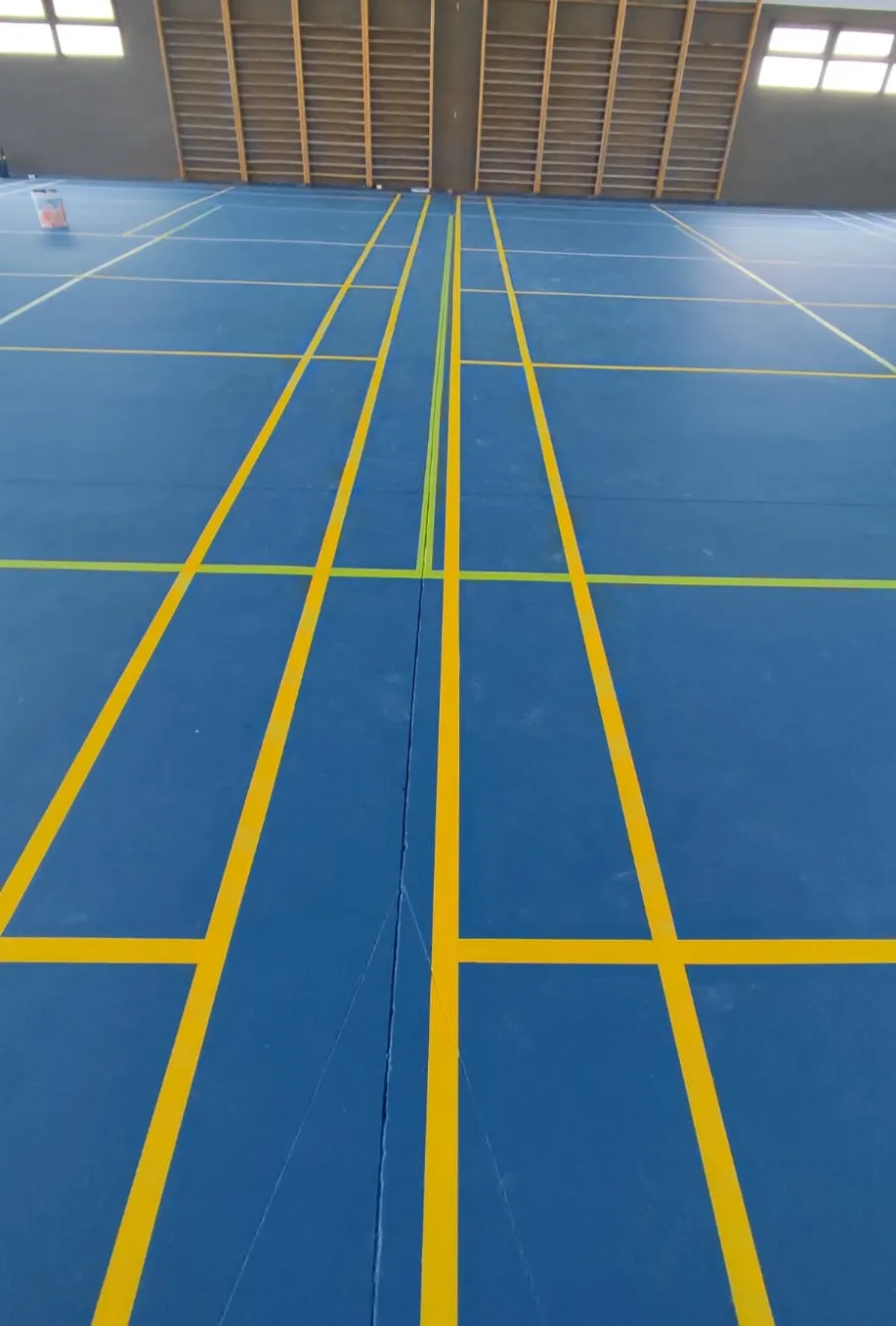 Pista deportiva cubierta de color azul con líneas amarillas y una pared de madera al fondo.