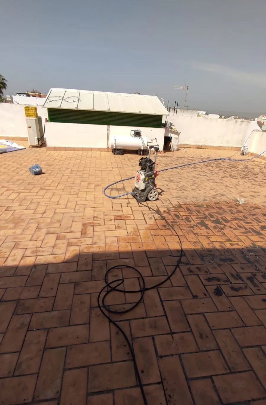 Un pequeño aspersor negro en un patio de ladrillos rocía agua hacia una pared blanca y un toldo verde.