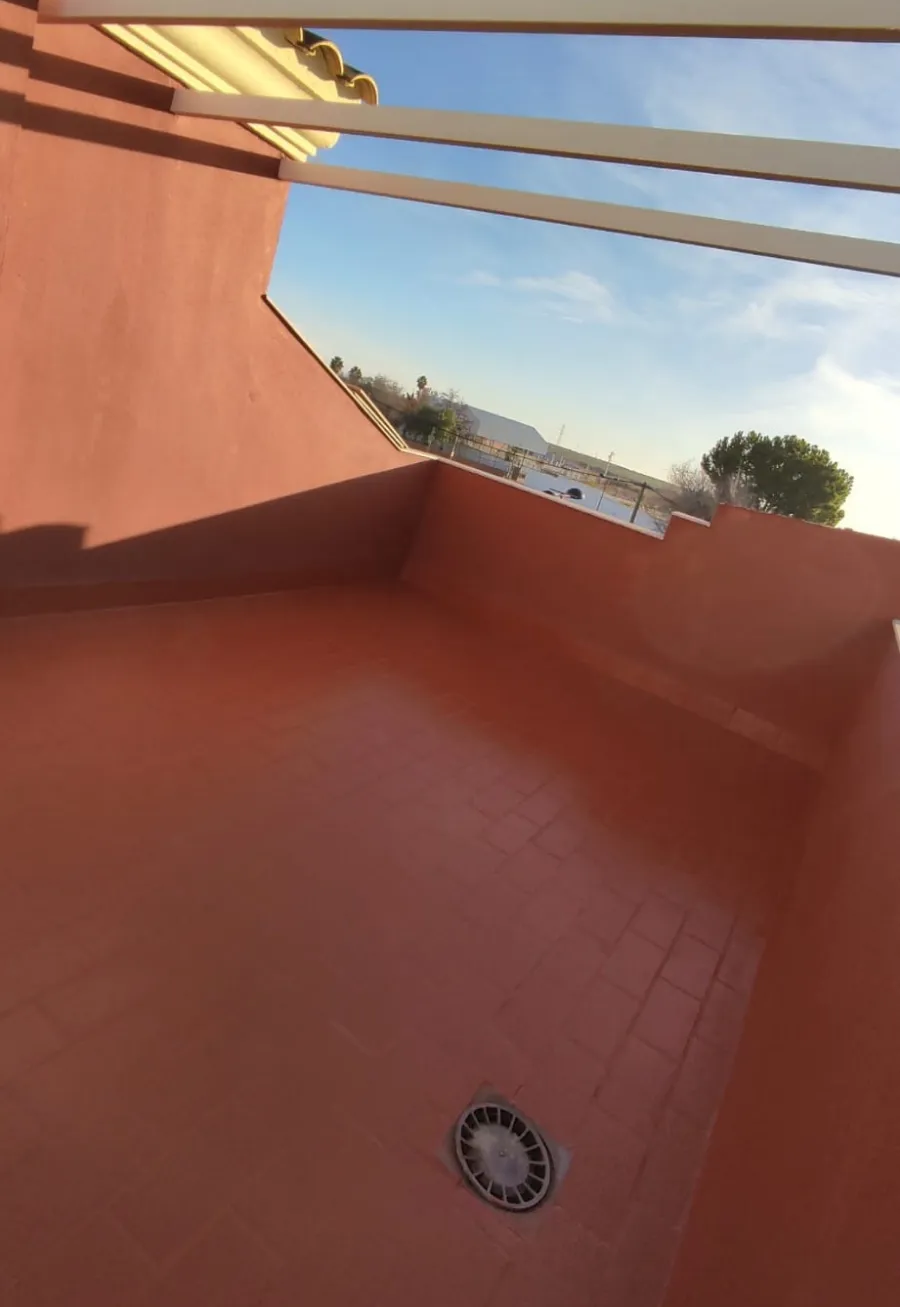 Balcón con baldosas rojas, paredes naranjas, cielo abierto y un pequeño desagüe redondo en el suelo.