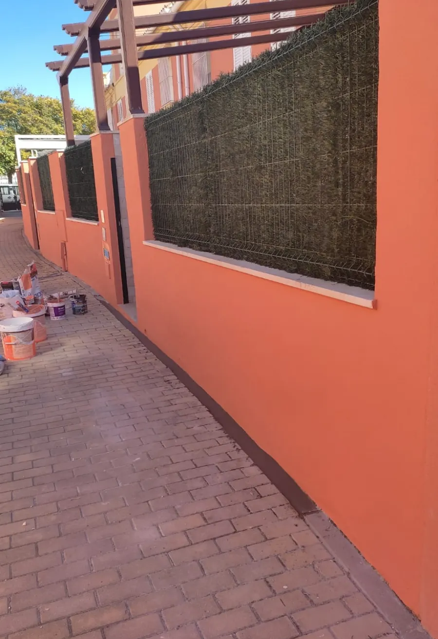 Pared naranja y sendero de ladrillos junto a un pasaje exterior vallado con un toldo metálico encima.