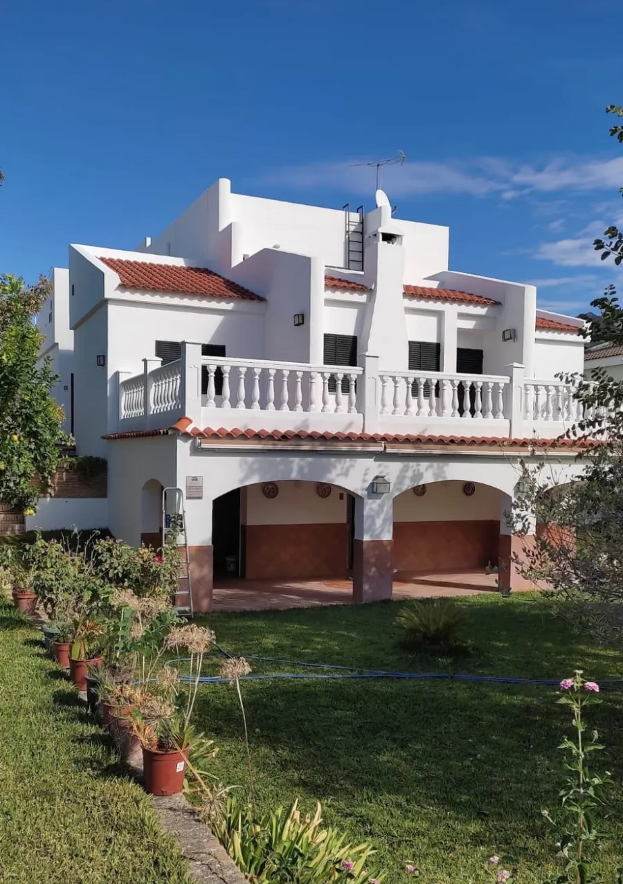 Estrecho pasillo exterior embaldosado con paredes blancas, laterales del edificio rojos y manguera enrollada en el suelo.