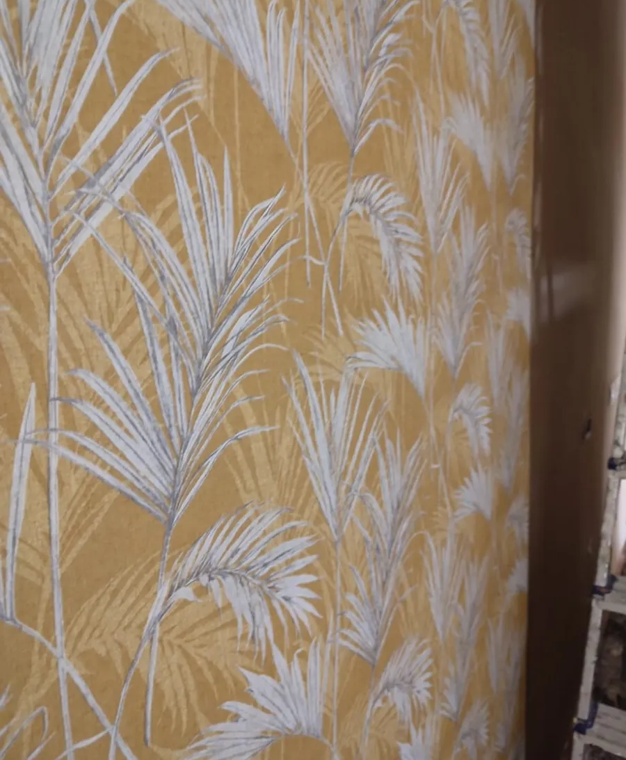 Pared amarilla con papel tapiz de estampado de hojas de palmera blancas y una puerta estrecha a la derecha.