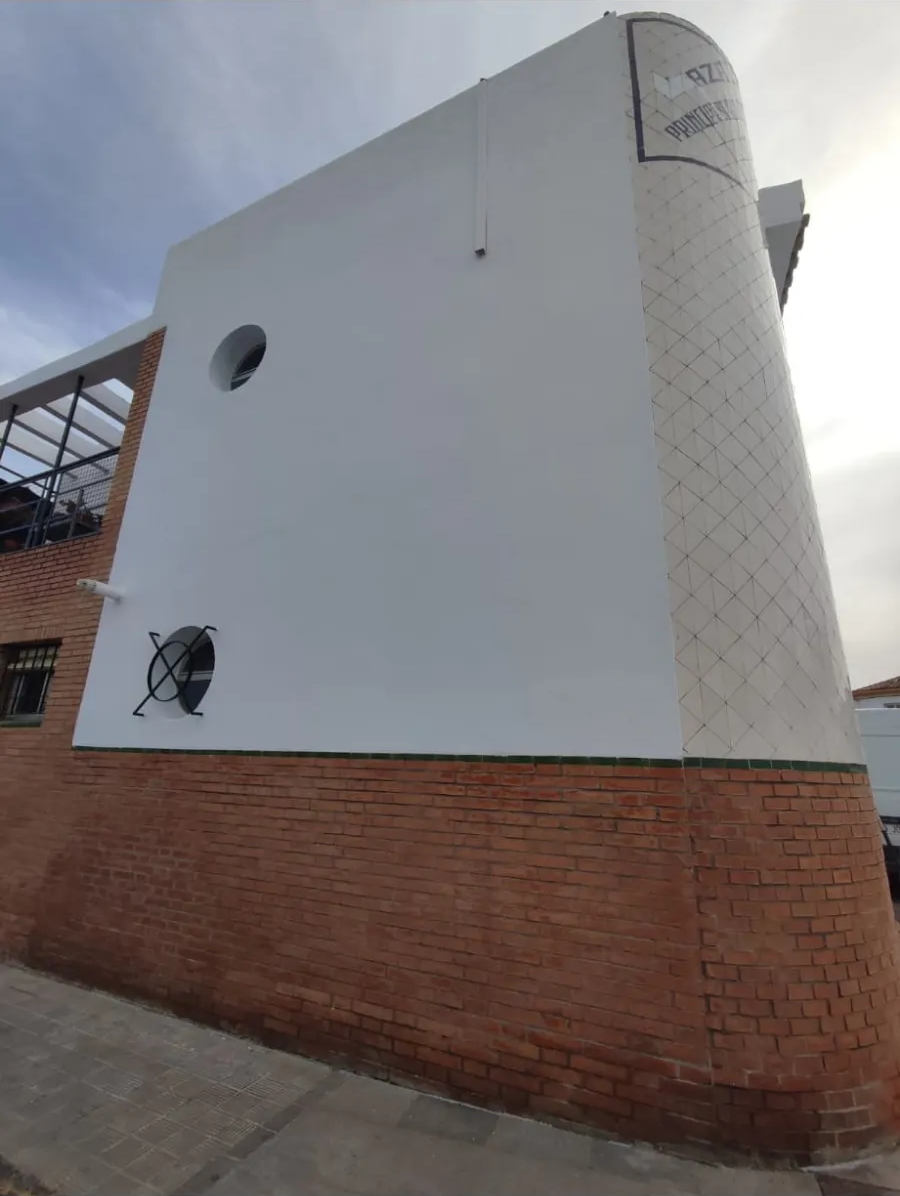 Edificio de fachada blanca y de ladrillo con ventanas redondas junto a una acera.