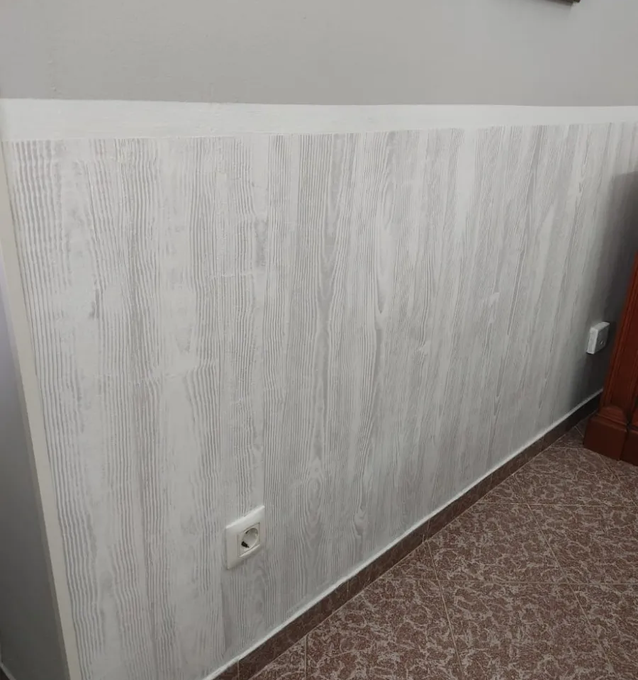 Pared blanca con revestimiento de madera texturizada, un enchufe y suelo alfombrado en un pasillo o habitación.