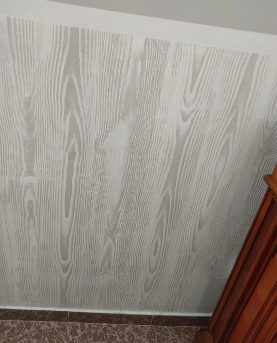 Panel de pared blanco estampado junto a molduras de madera marrón y suelo enmoquetado.