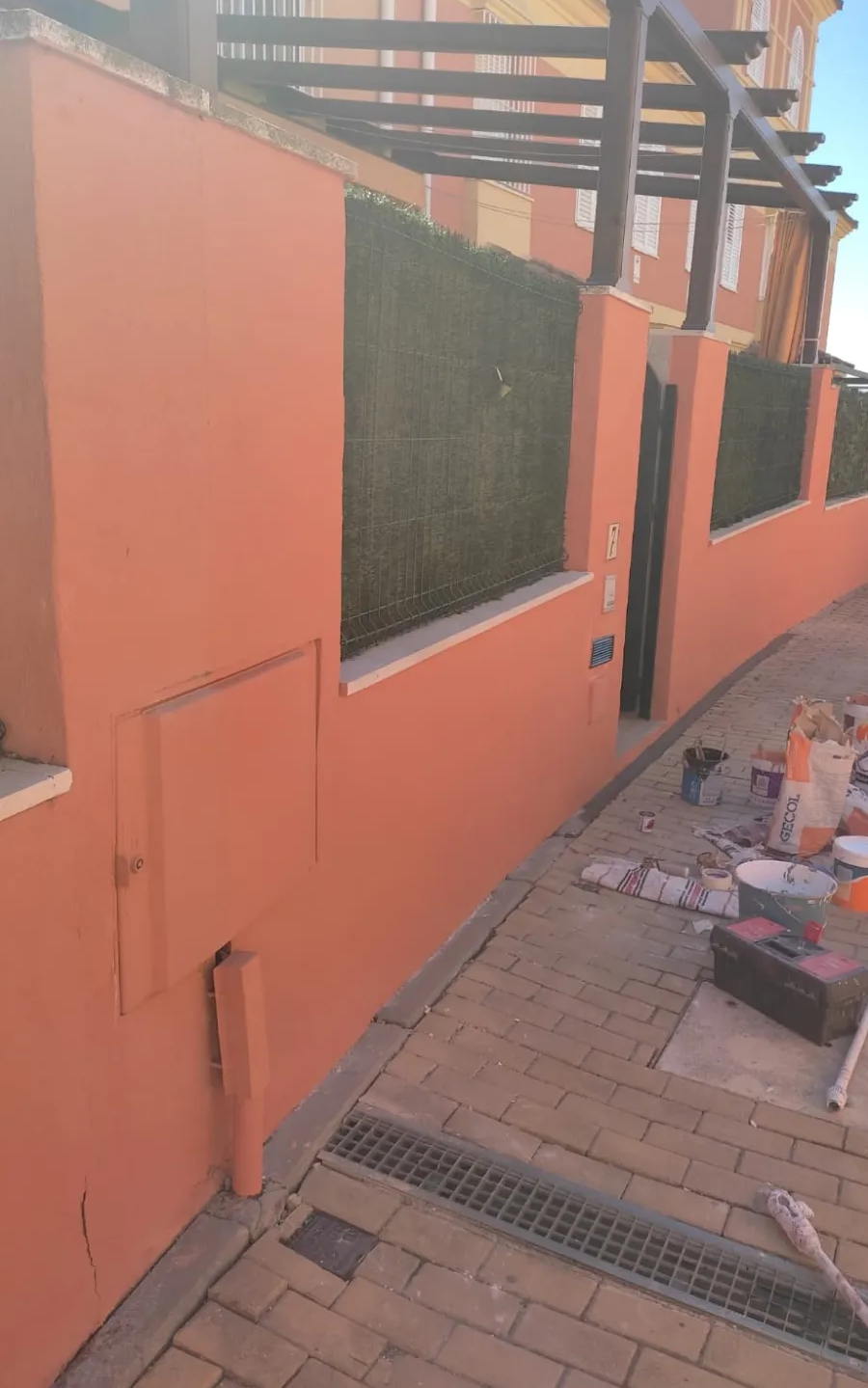 Edificio de color naranja con fachada acristalada, escalera metálica y pasarela de ladrillos a lo largo del lateral.
