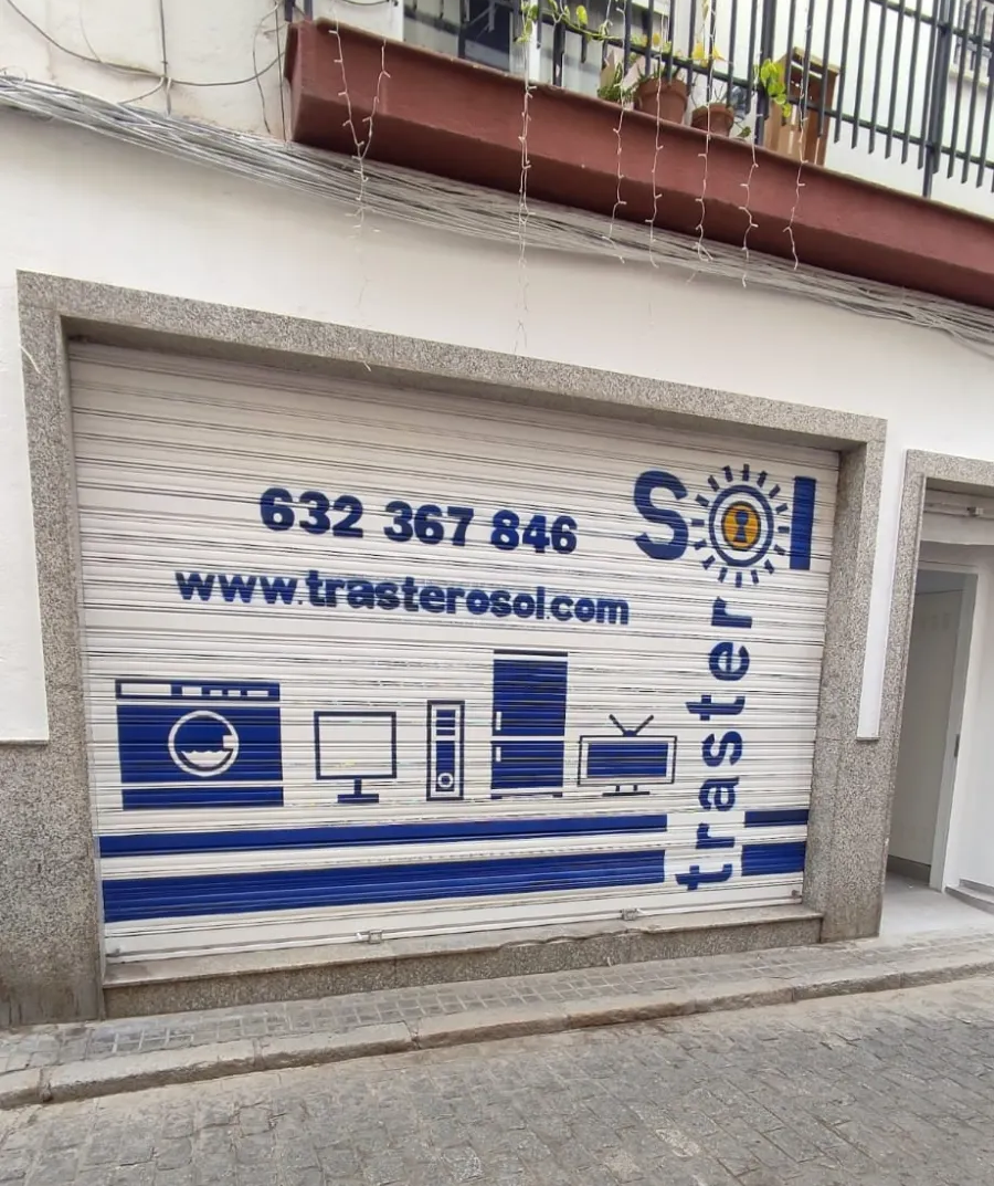 Local comercial cerrado con persiana metálica blanca, letrero azul y texto en español en una esquina de la calle.