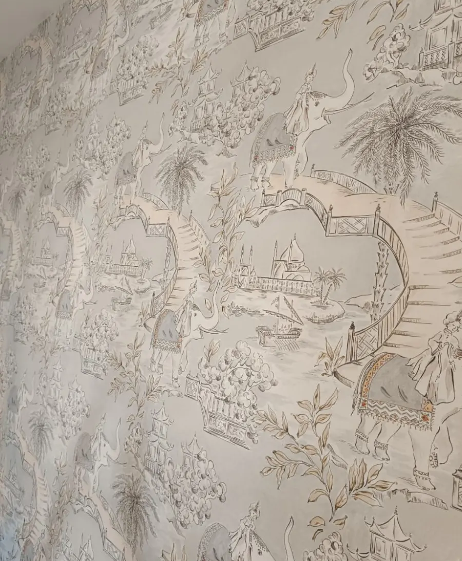 Pared beige con un papel pintado de estampado detallado con motivos de pájaros, hojas y flores.