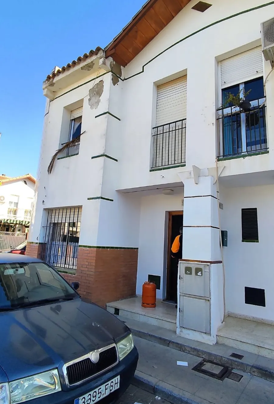 Casa blanca de dos plantas con un coche aparcado delante y una persona en la puerta.