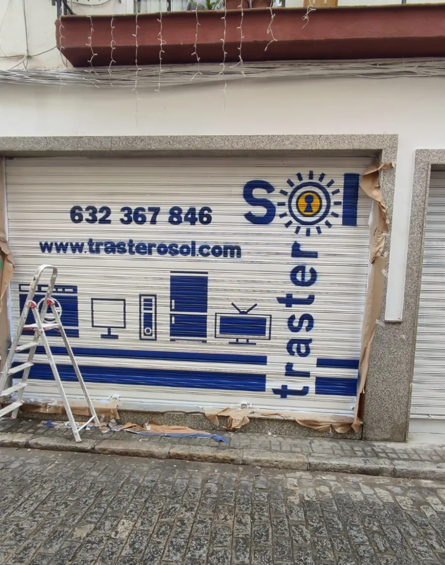 Escaparate cerrado con el logotipo de Traster, número de teléfono y sitio web; escalera a la izquierda en el exterior.