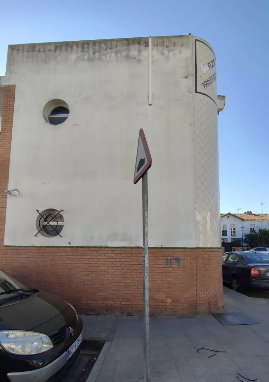 Lateral de un edificio beige y de ladrillo con una señal de aparcamiento y coches aparcados a lo largo de una calle.