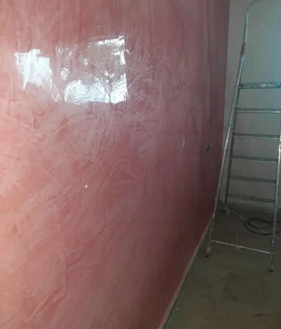 Pared interior pintada de rosa con una escalera plateada apoyada contra ella cerca de la esquina.