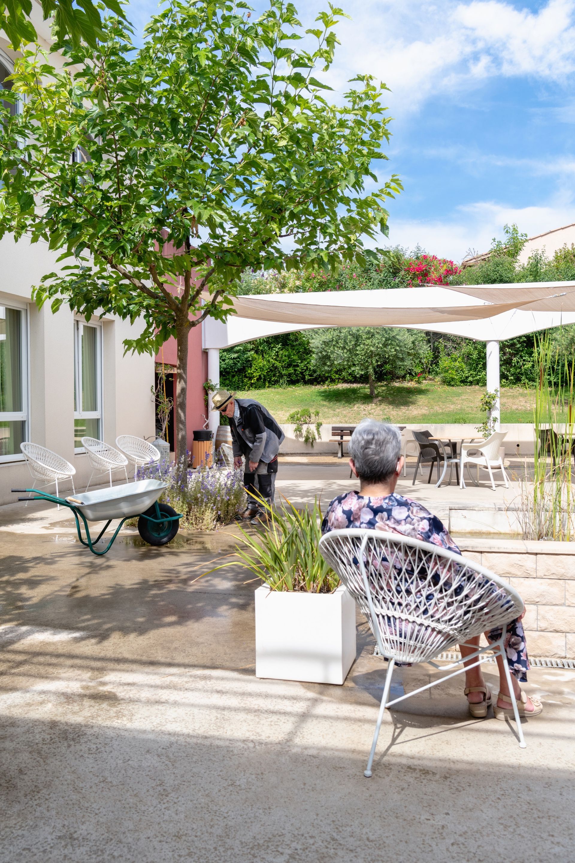 Une femme assise dans un fauteuil et un homme qui jardine