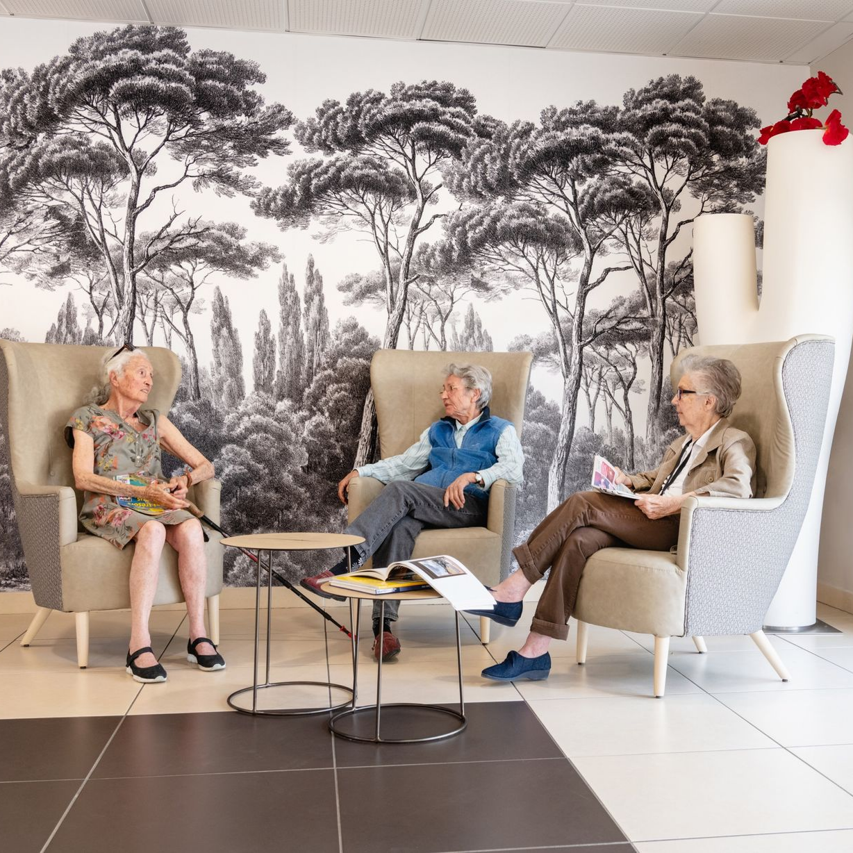 Trois personnes, dont une personne en fauteuil roulant, assises à une table de jardin, sourient et discutent.