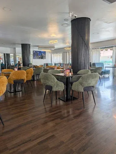 Salón moderno con sillones de terciopelo, suelos de madera oscura y grandes ventanales en un luminoso vestíbulo