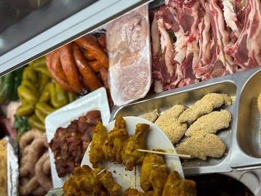 Variedad de carnes crudas y cocinadas, así como productos empanizados, expuestos en una vitrina tipo charcutería.