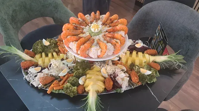 Plato decorativo de mariscos con camarones, cangrejo, guarnición de frutas y piña en el centro sobre una mesa.