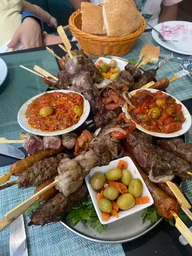 Plato de brochetas a la parrilla con salsas para mojar y verduras encurtidas sobre una mesa.