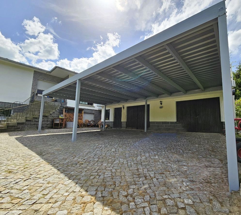 Ein Carport vor einem Haus mit einer gepflasterten Auffahrt