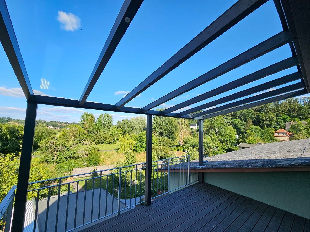 Ein Balkon mit Glasdach und Blick auf einen Wald.