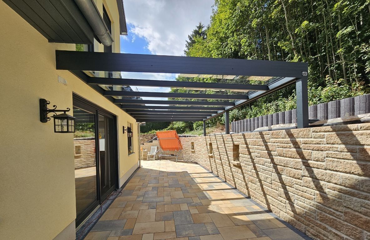 Eine Terrasse mit Pergola und Backsteinmauer vor einem Haus.