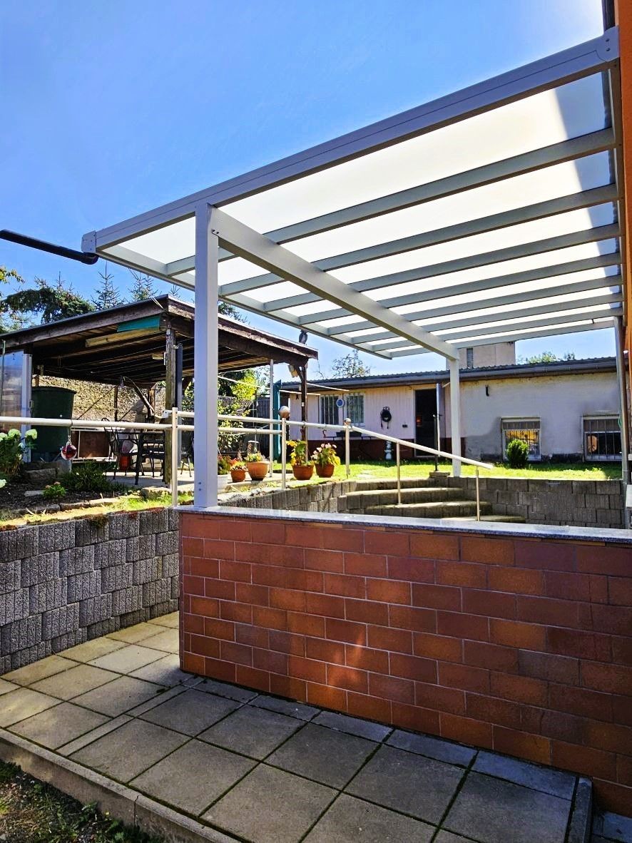Eine Terrasse mit Pergola und Backsteinmauer vor einem Haus.