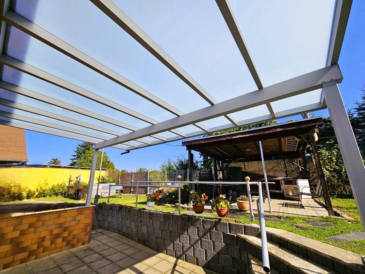 Eine Terrasse mit einem Baldachin darüber und einem Haus im Hintergrund.