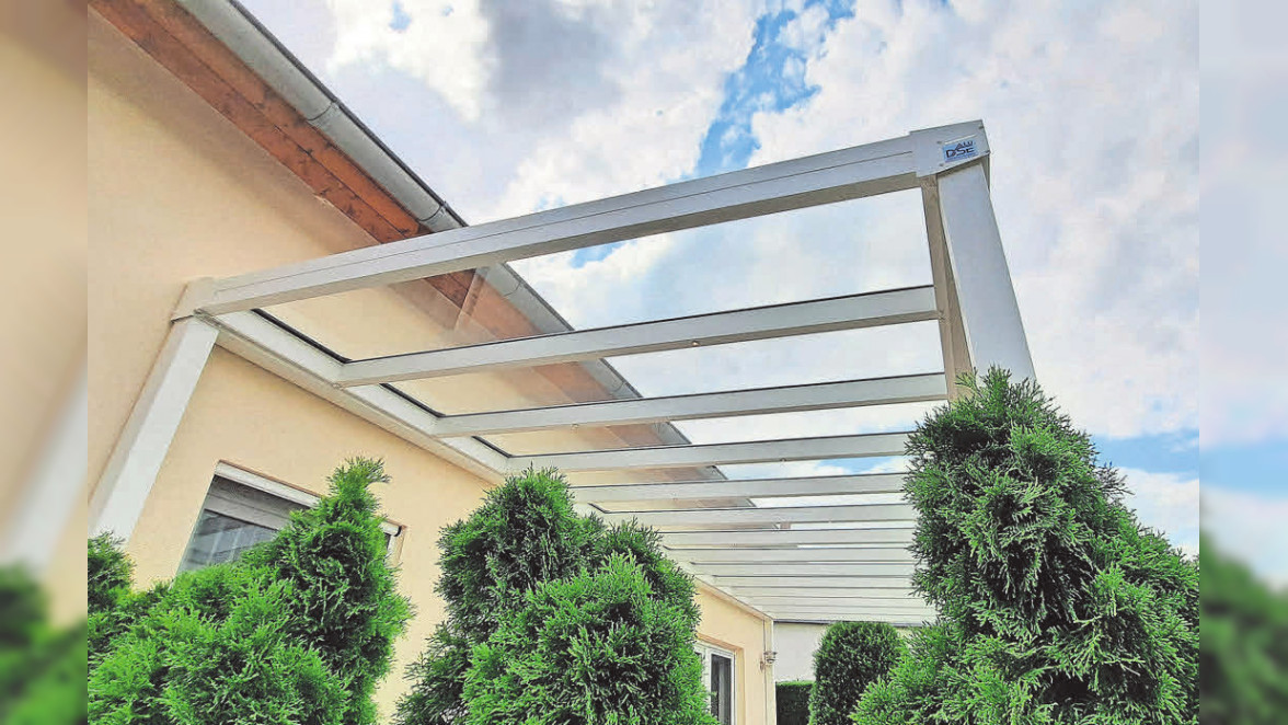 Eine weiße Pergola steht vor einem von Bäumen umgebenen Haus.