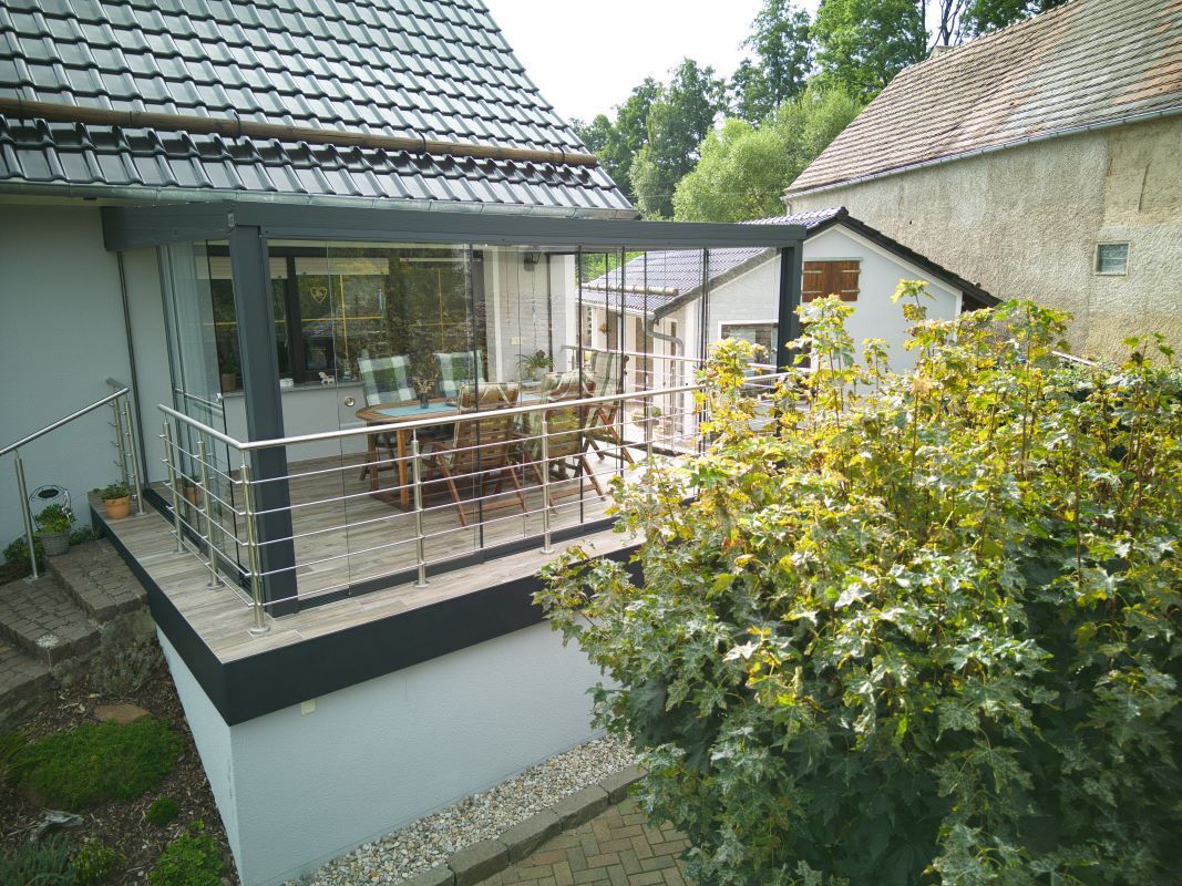 Vor einem Haus befindet sich ein Balkon mit Tisch und Stühlen.
