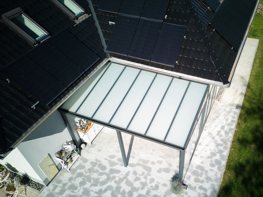 Eine Luftaufnahme eines Hauses mit einem Vordach und Solarmodulen auf dem Dach.