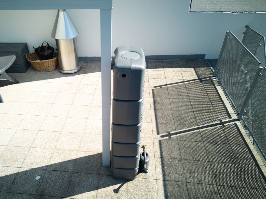 Ein grauer Container steht auf einer Terrasse neben einem Tisch