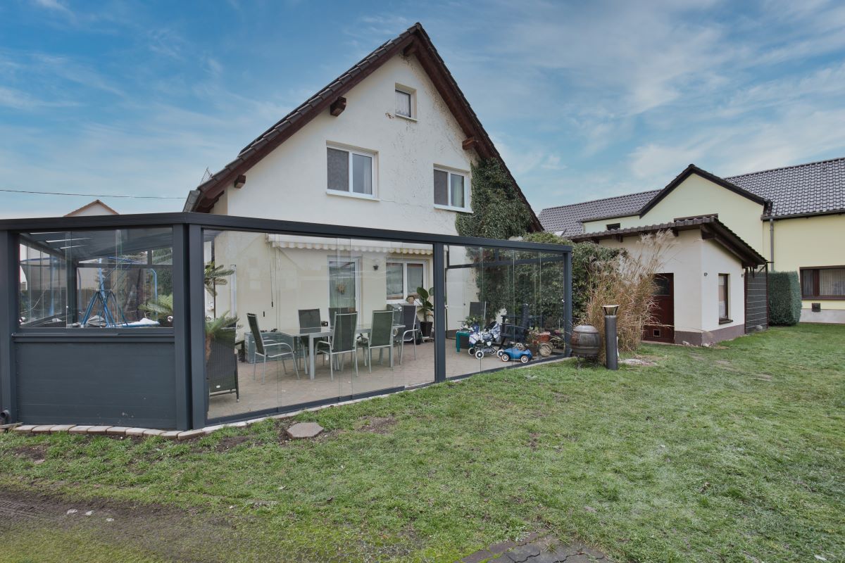 Ein Haus mit Terrasse und davor liegender Pergola.