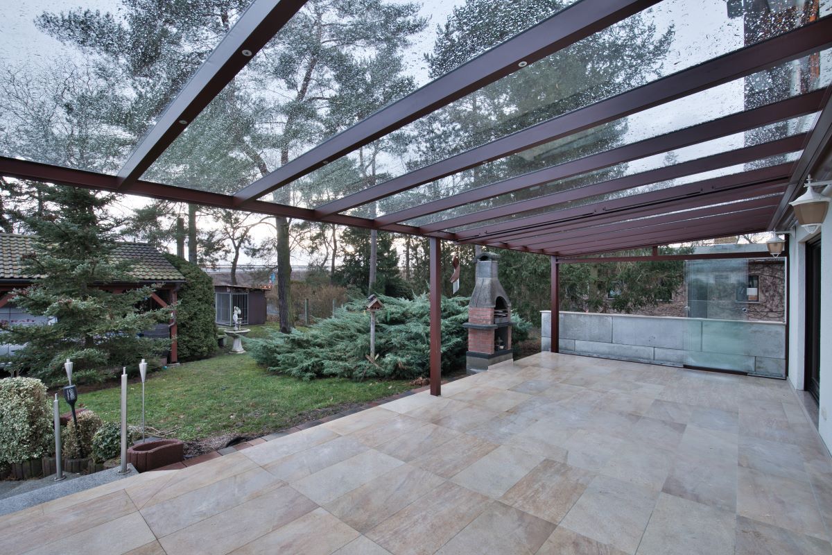 Eine große Terrasse mit Glasdach und Grillmöglichkeit.