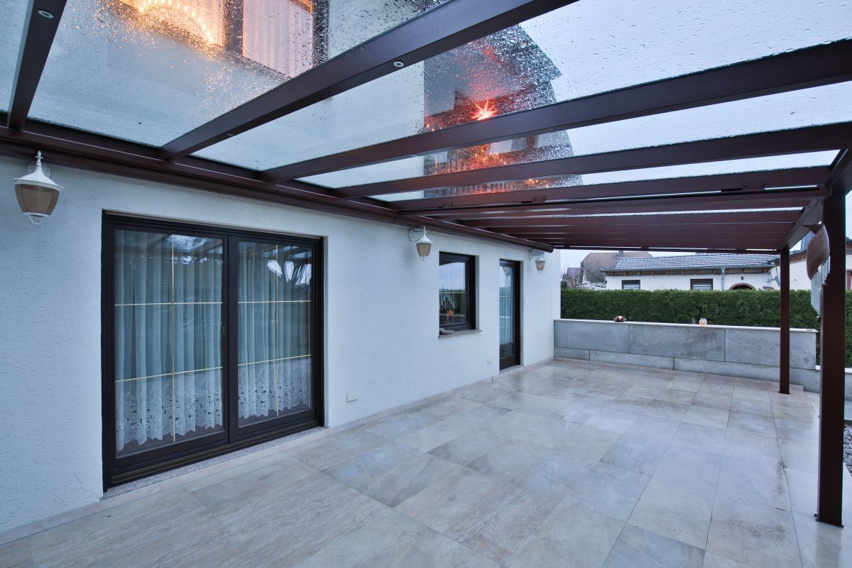 Eine Terrasse mit Glasdach und Holzpergola.