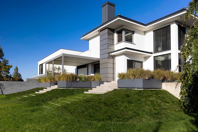 Auf einem üppig grünen Hügel steht ein großes weißes Haus.