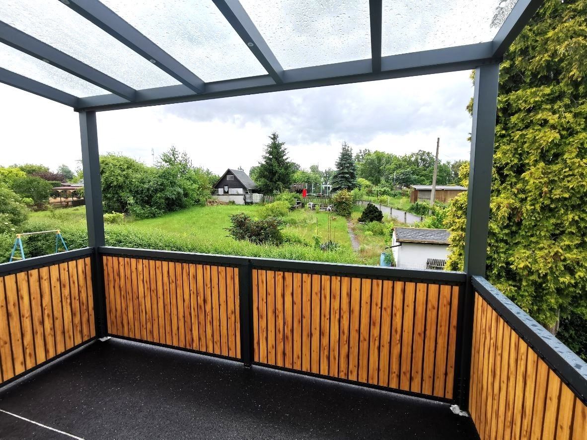 Ein Balkon mit Holzgeländer und transparentem Dach.