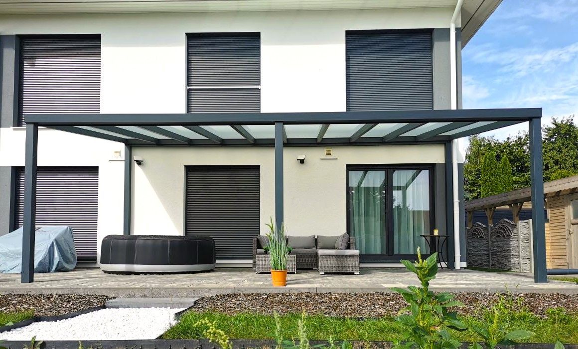 Ein Haus mit Terrasse und davor liegender Pergola.