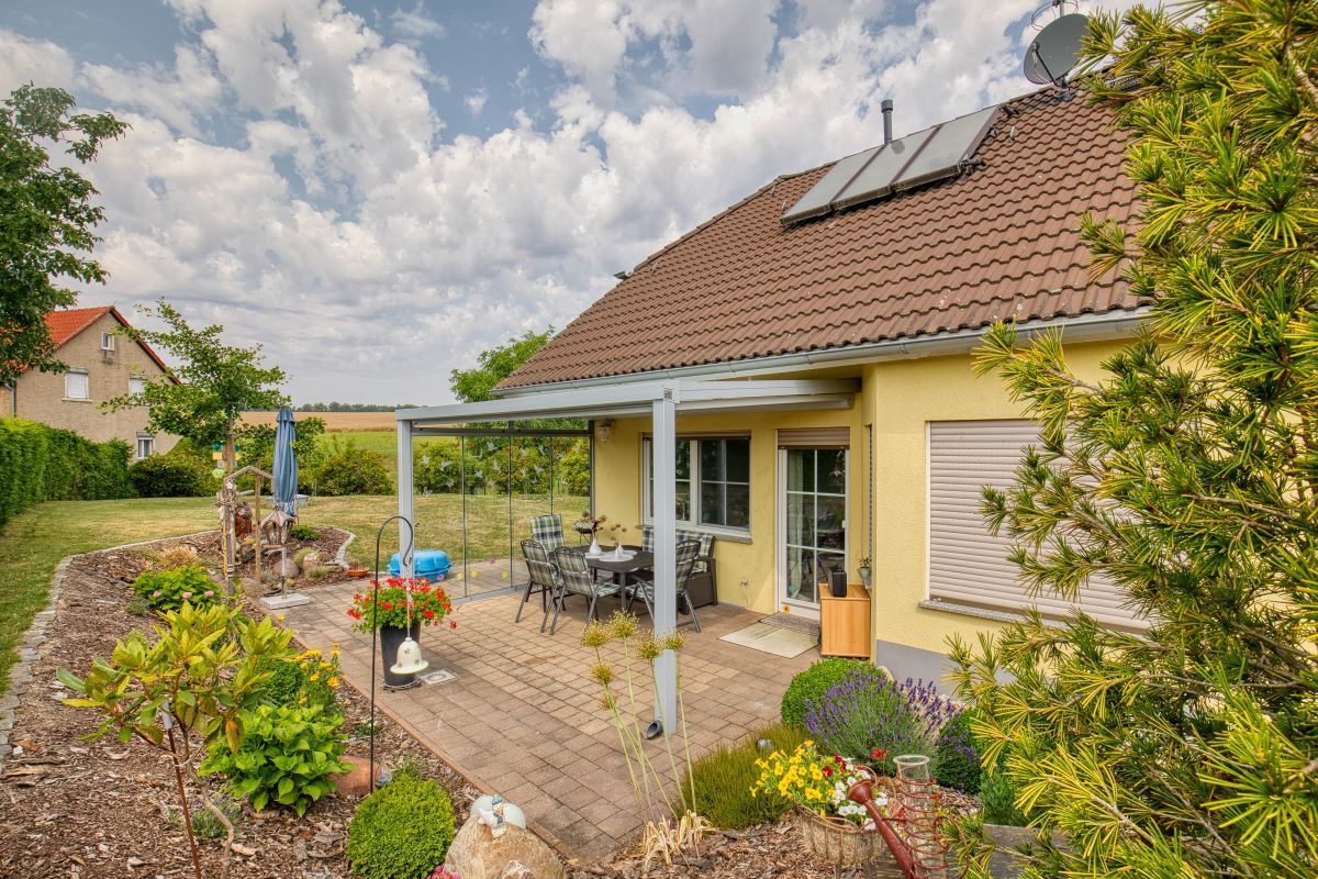 Ein gelbes Haus mit einer Pergola und einer Terrasse davor.
