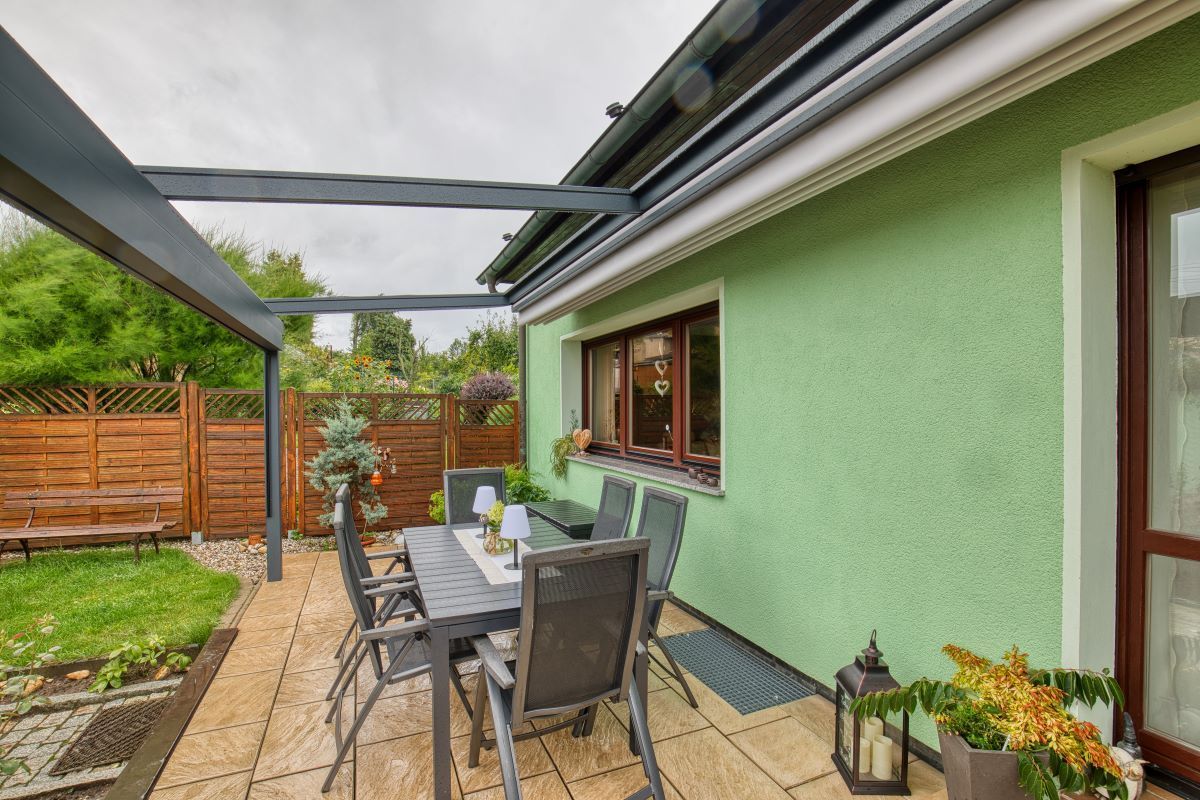 Ein Gewächshaus mit einer Terrasse mit Tisch und Stühlen unter einer Pergola.