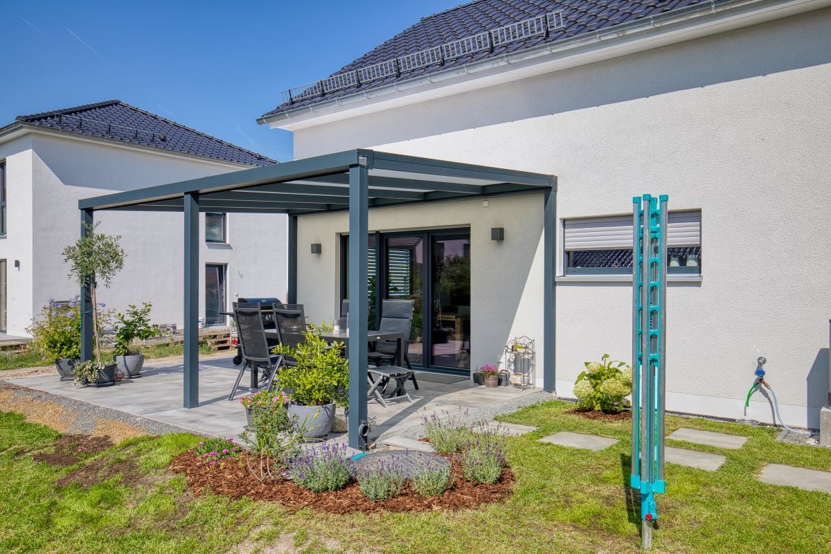 Ein weißes Haus mit einer Terrasse und einer Pergola davor.