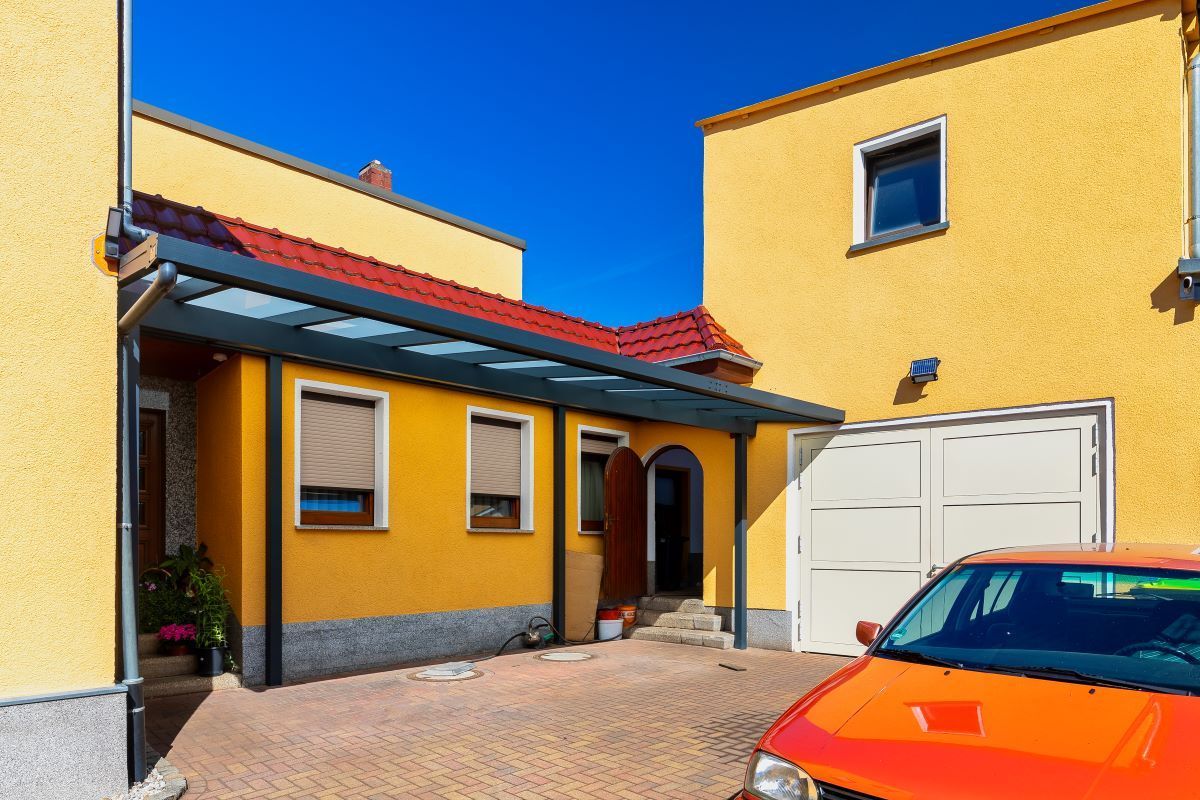 Ein orangefarbenes Auto steht vor einem gelben Haus