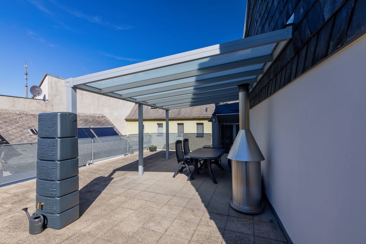 Eine Terrasse mit Tisch und Stühlen unter einem Baldachin und einer Gießkanne.