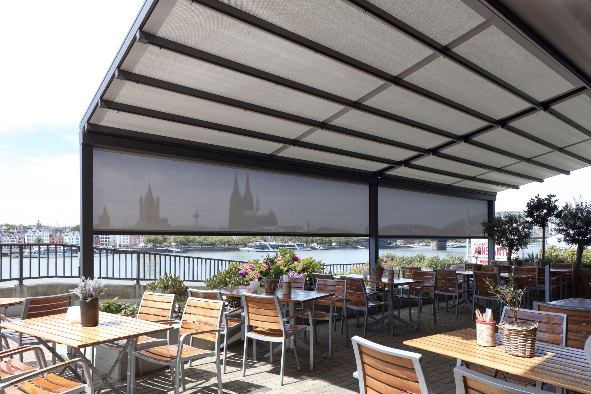 Ein Restaurant mit Tischen und Stühlen unter einem Vordach mit Blick auf ein Gewässer