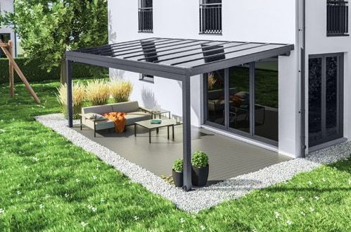 Eine Terrasse mit Pergola und Couch vor einem Haus.