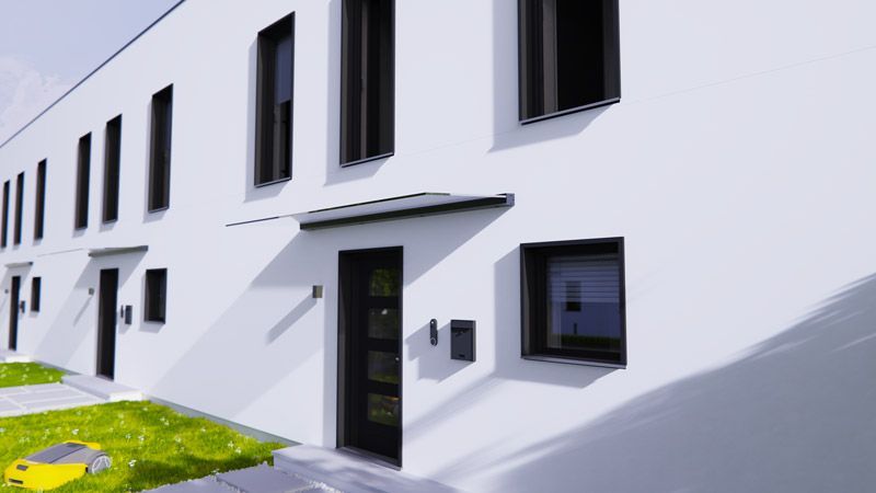 Ein weißes Gebäude mit schwarzen Fenstern und einem gelben Rasenmäher davor.